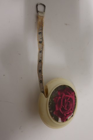 Målebånd i en runde holder, prydet med en rose, målebåndet trækkes udMålebåndet er fra den gode gamle tidPræget: "Dean Measure" Made in England